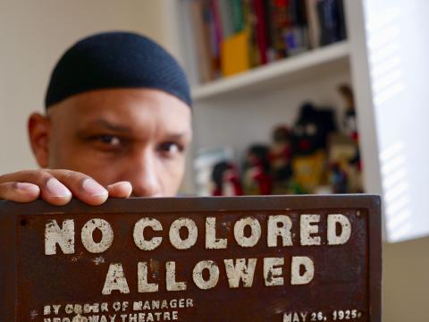 Dr. Khalid El-Hakim holding an antique sign that says "No Colored Allowed"