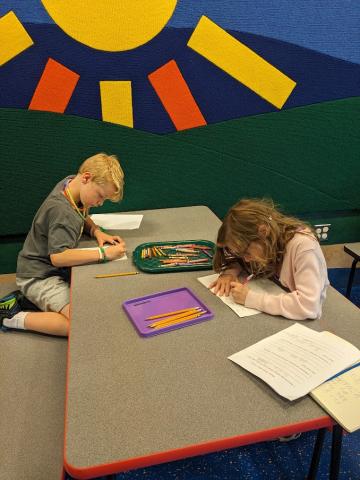 Two children writing while sitting at the table.