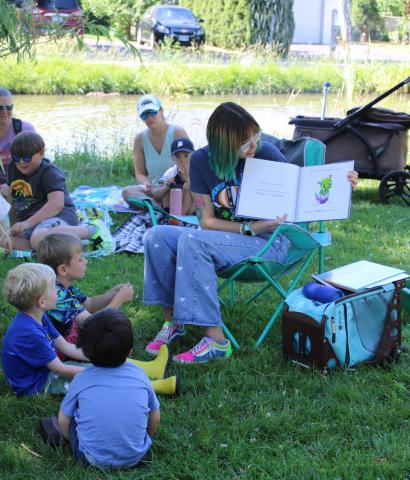 Librarian sitting in a lawn chair, reading a story to group of children outside
