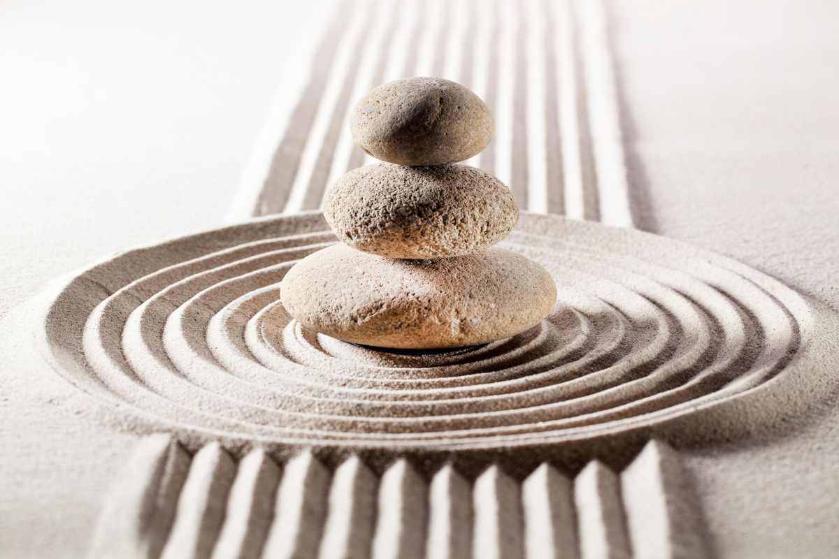 A stack of three rocks on top of smooth sand with symmetrical waves